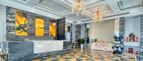 Eine Hotelhalle mit einer Rezeption, einem gemusterten Boden und einer Kristallleuchtre.
