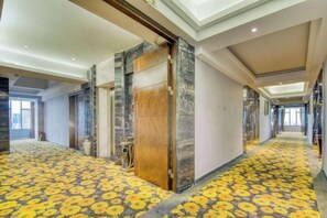 A hotel corridor with a patterned carpet, marble walls, and a wooden door. - Xinyi Hotel (Dongguan)