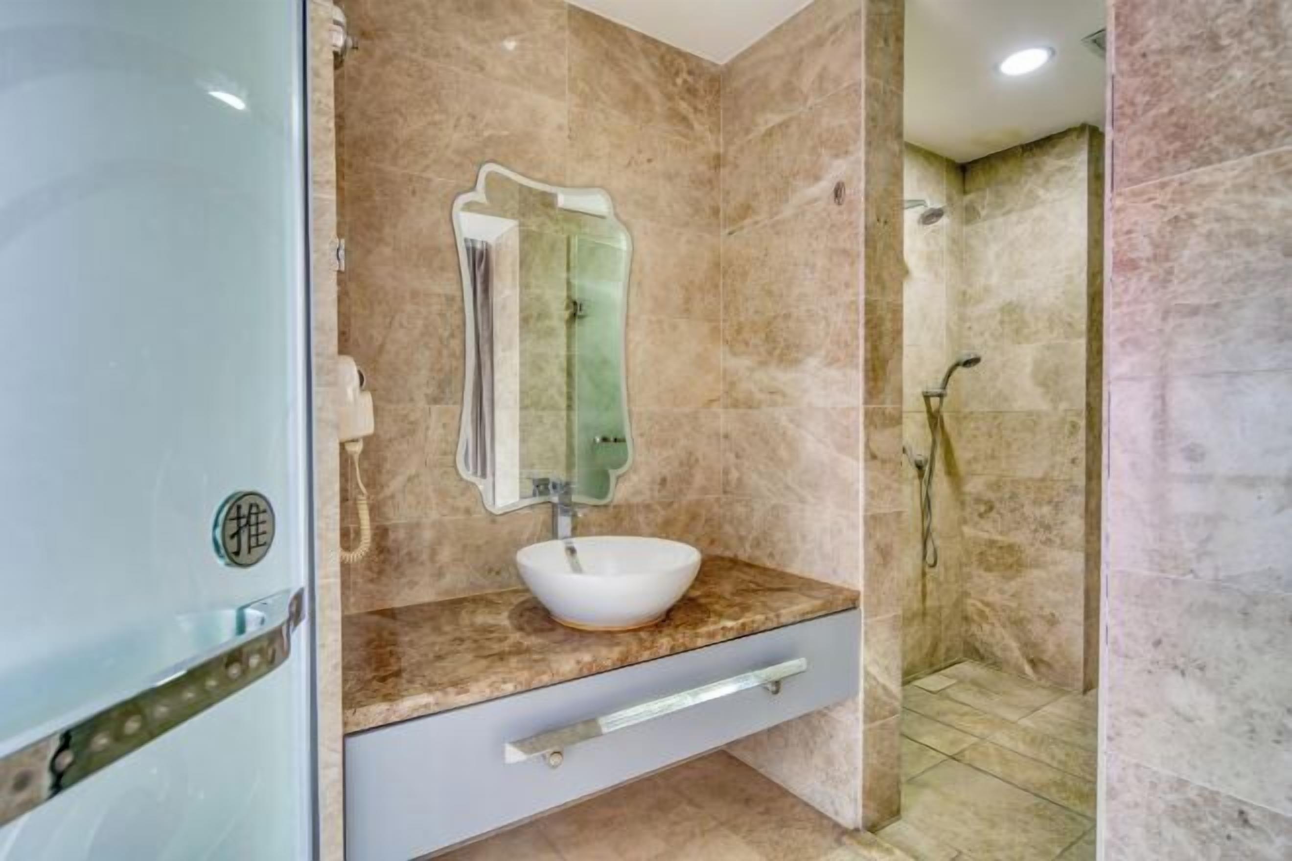 A bathroom with a marble sink, a mirror, and a shower area.