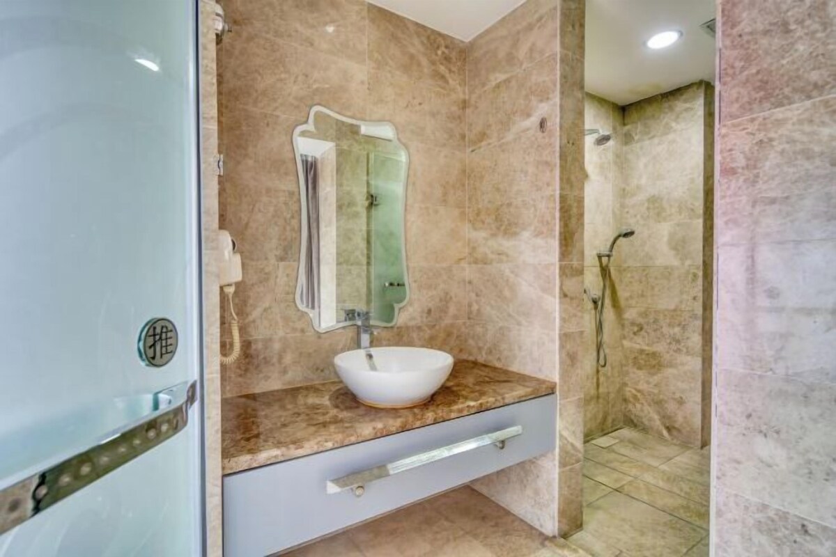 A bathroom with a marble sink, a mirror, and a shower area.