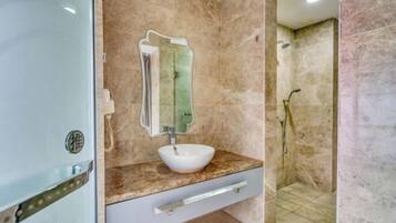 A bathroom with a marble sink, a mirror, and a shower area.