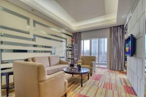 A hotel room with a sofa, armchair, coffee table, and a television. - Xinyi Hotel (Dongguan)