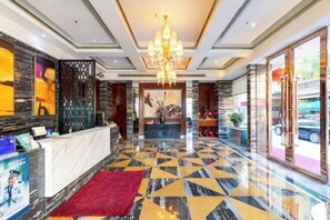 A hotel lobby with a reception desk, a chandelier, a patterned floor, and a large window with a view of the outside. - Xinyi Hotel (Dongguan)