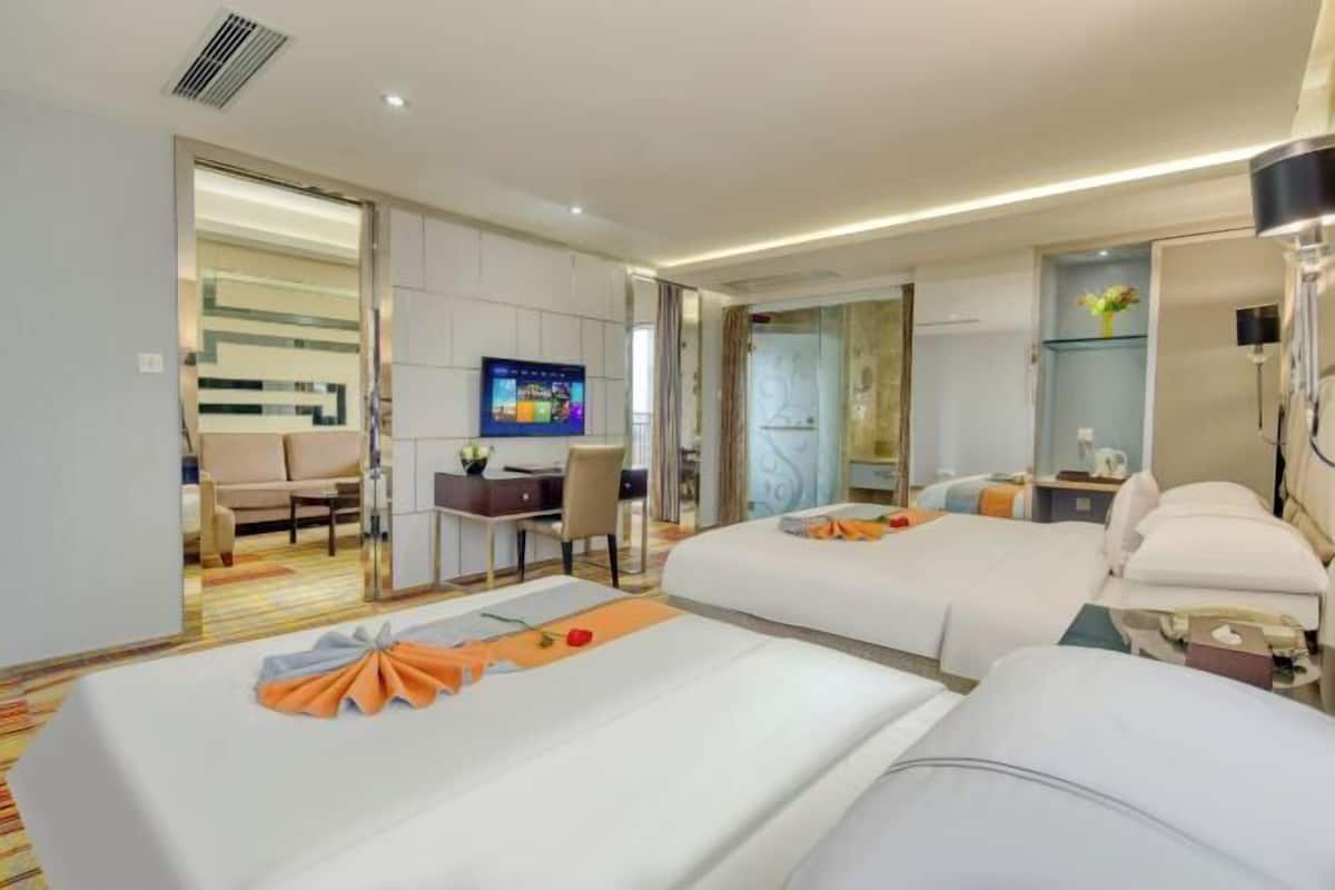 A hotel room with two beds, a desk with a chair, a television, and a bathroom visible through an open door.