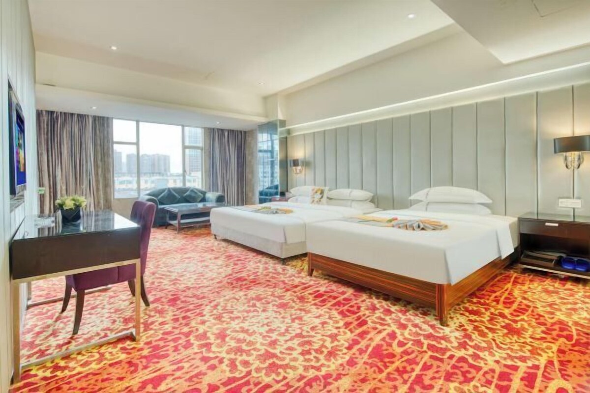 A hotel room with two beds, a desk, a chair, and a large window.