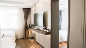 Una habitación de hotel con una cama, televisión montada en la pared, mesita de noche y una ventana con cortinas.