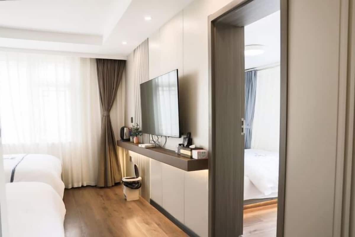 A hotel room with a bed, a TV mounted on the wall, a bedside table, and a window with curtains.