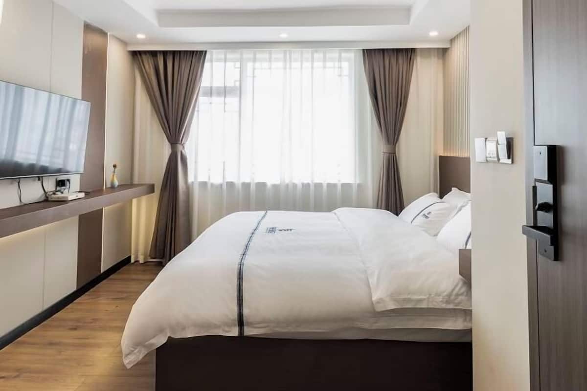 A hotel room with a bed, a TV, a desk, and a window with curtains.