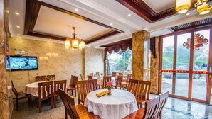 Un comedor con mesas redondas y sillas de madera, un televisor montado en la pared y un amplio ventanal que da al exterior.