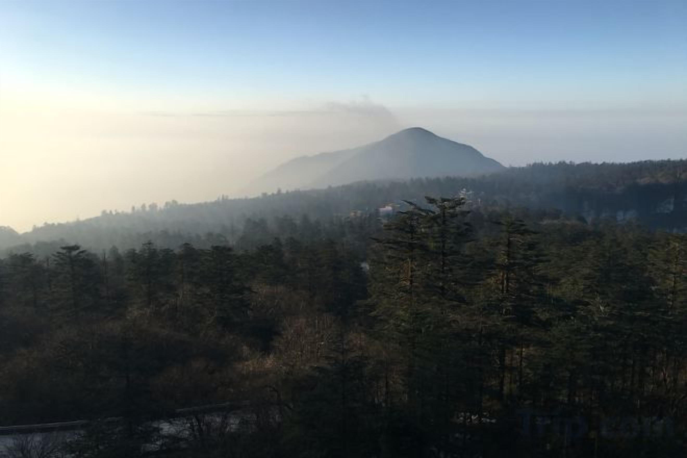 Paisagem montanhosa com área arborizada e céu limpo.
