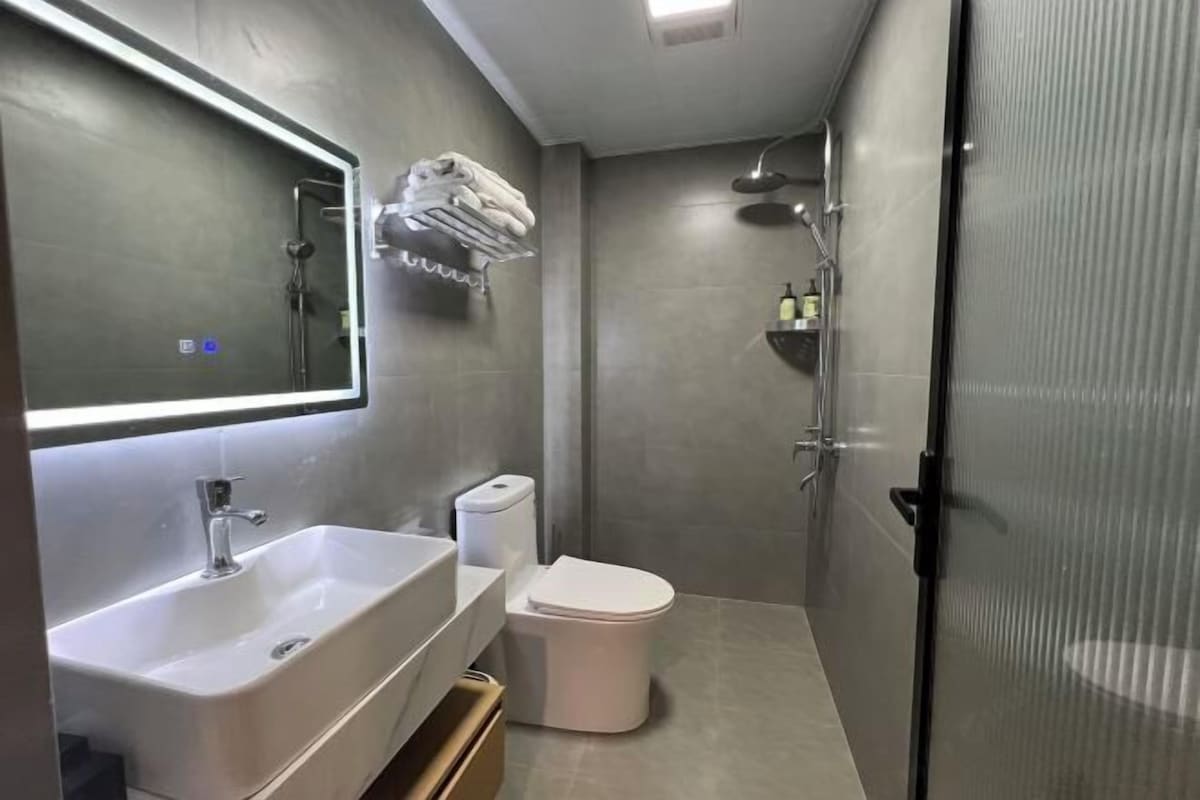 Un baño moderno con un espejo grande, un lavabo, un inodoro y una zona de ducha.