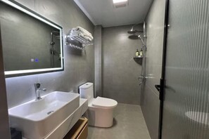 A modern bathroom with a large mirror, a sink, a toilet, and a shower area. - Foguang Hotel (Emeishan City)