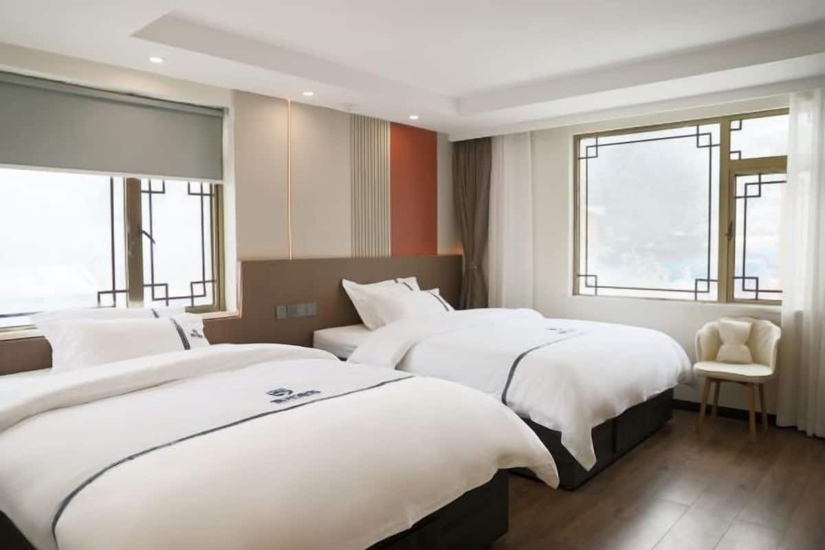 A hotel room with two beds, a chair, and large windows.
