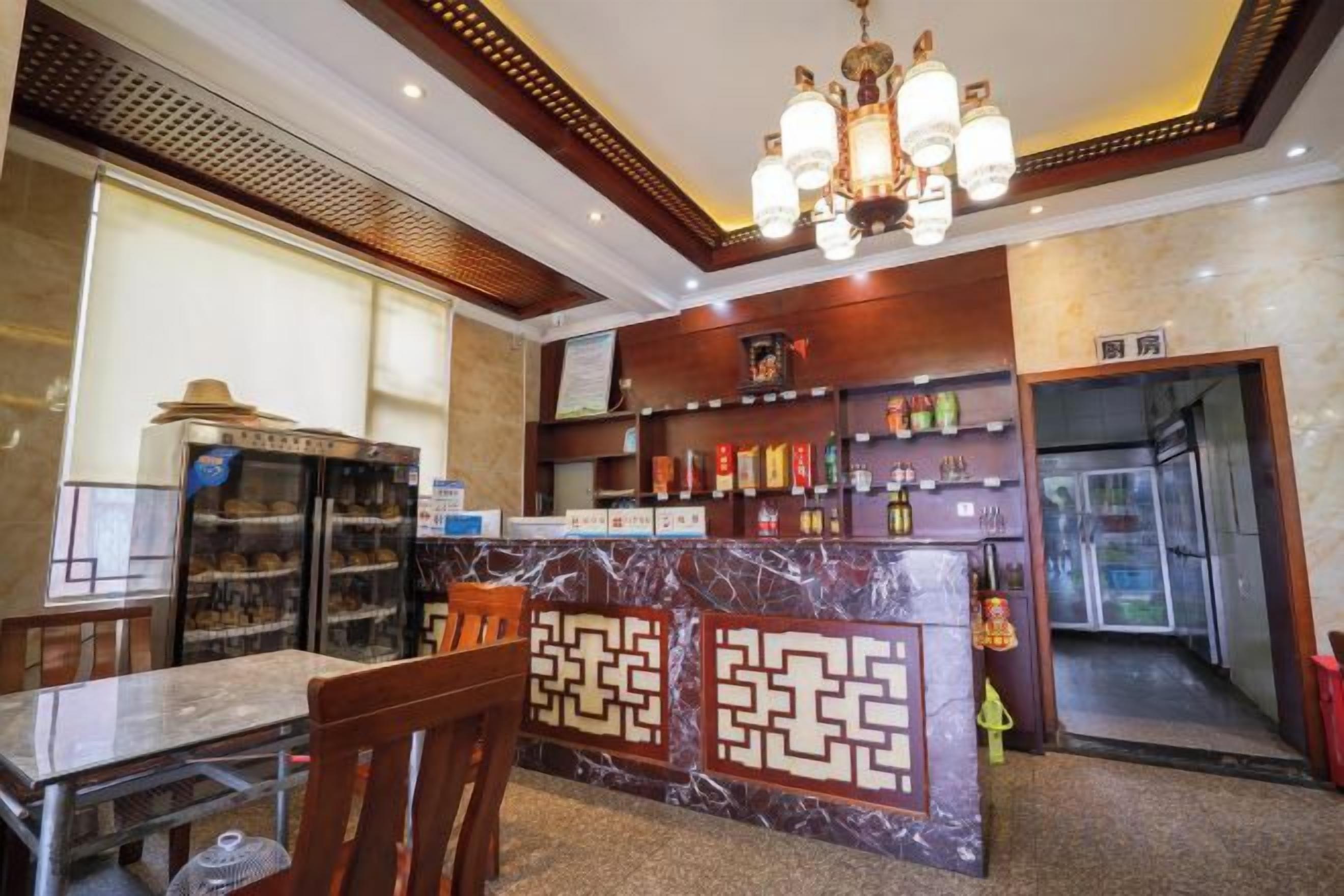 A hotel lobby with a marble reception desk, a dining area with a table and chairs, and a bar area with shelves of bottles.