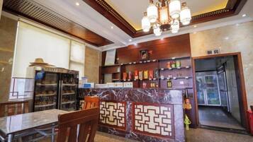 A hotel lobby with a marble reception desk, a dining area with a table and chairs, and a bar area with shelves of bottles.