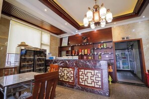 A hotel lobby with a marble reception desk, a dining area with a table and chairs, and a bar area with shelves of bottles.