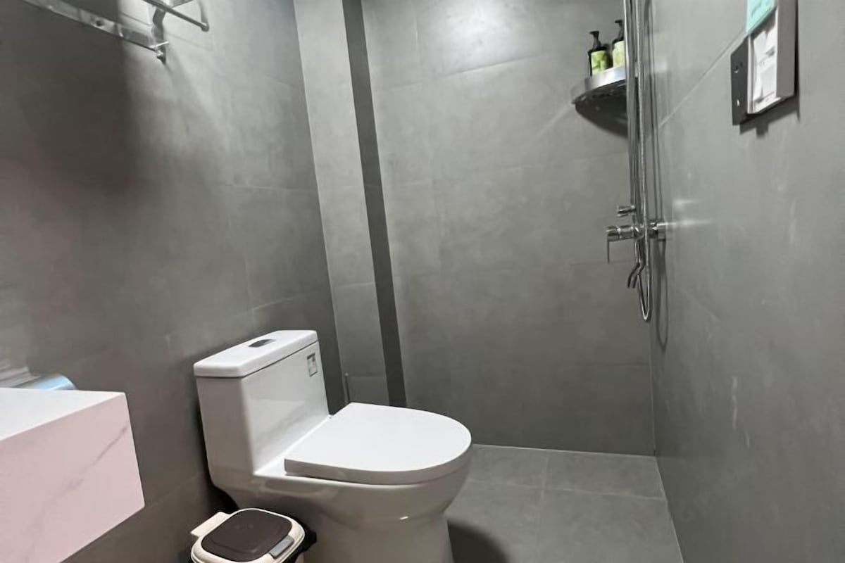 Un baño moderno con inodoro, ducha y un pequeño estante con artículos de aseo.