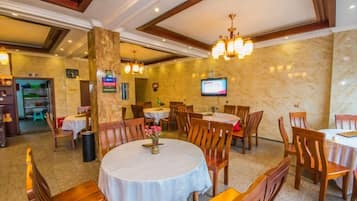 A restaurant with round tables, wooden chairs, and a chandelier.