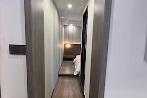 Un pasillo estrecho y moderno con suelo de madera y paredes blancas, que conduce a un dormitorio con cama y mesita de noche.