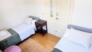 Una habitación pequeña y limpia con dos camas individuales, una mesita de noche de madera, una pequeña mesa y una puerta con cerradura.