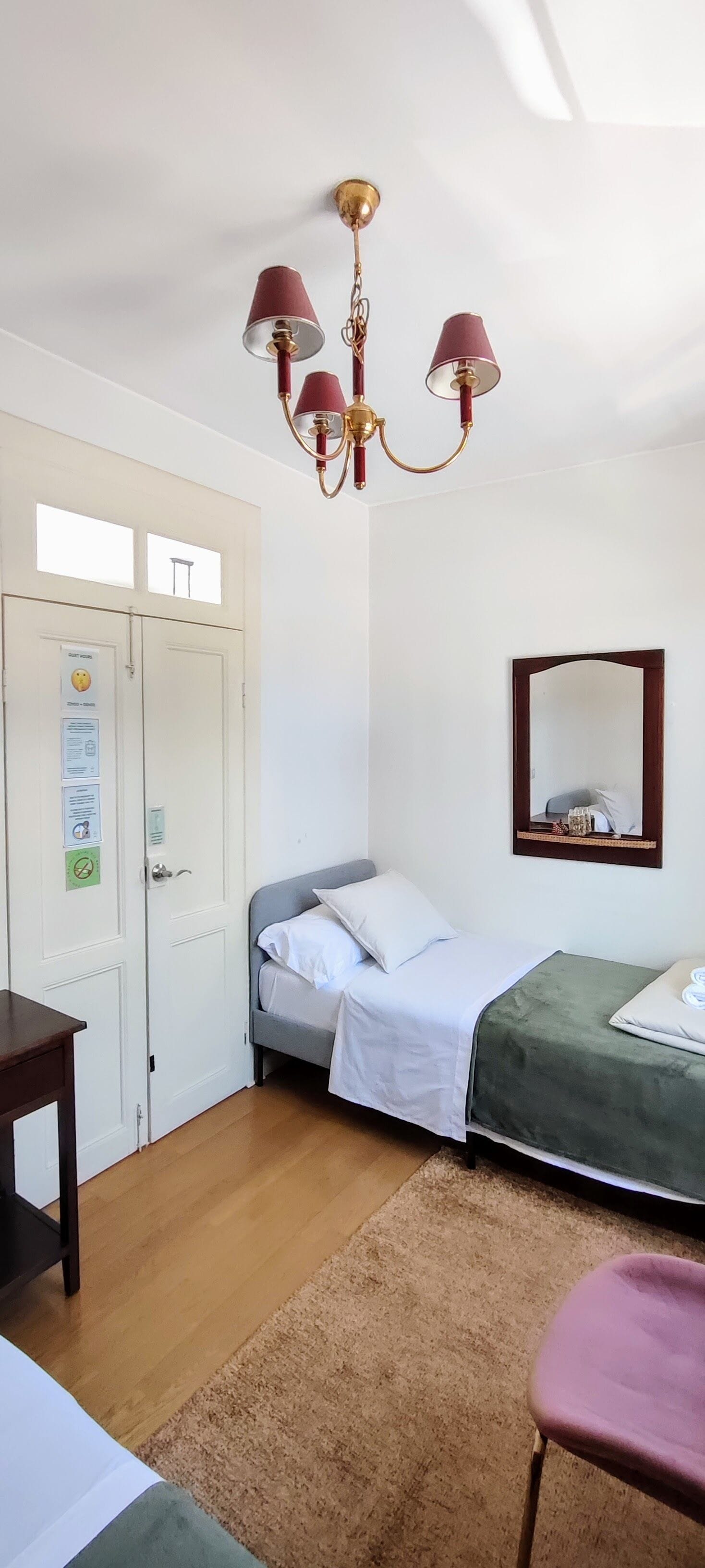 A room with two beds, a wooden floor, a desk, a chair, a chandelier, and a mirror.