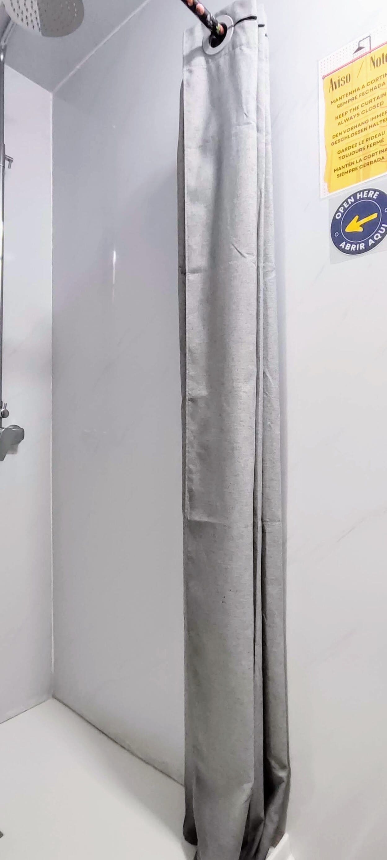 A bathroom with a shower curtain, a wall-mounted towel rack, and a sign with instructions.