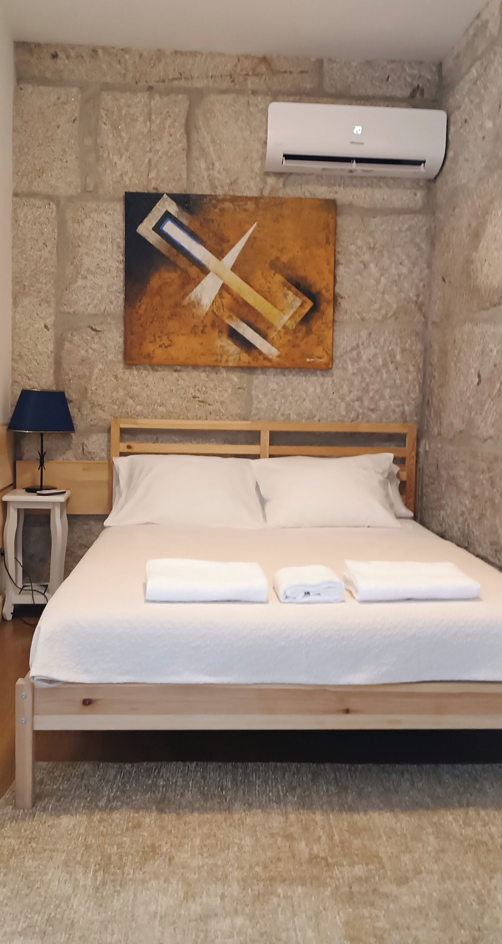 Una cama bien hecha con ropa blanca y toallas, cabecera de madera y pared de piedra.