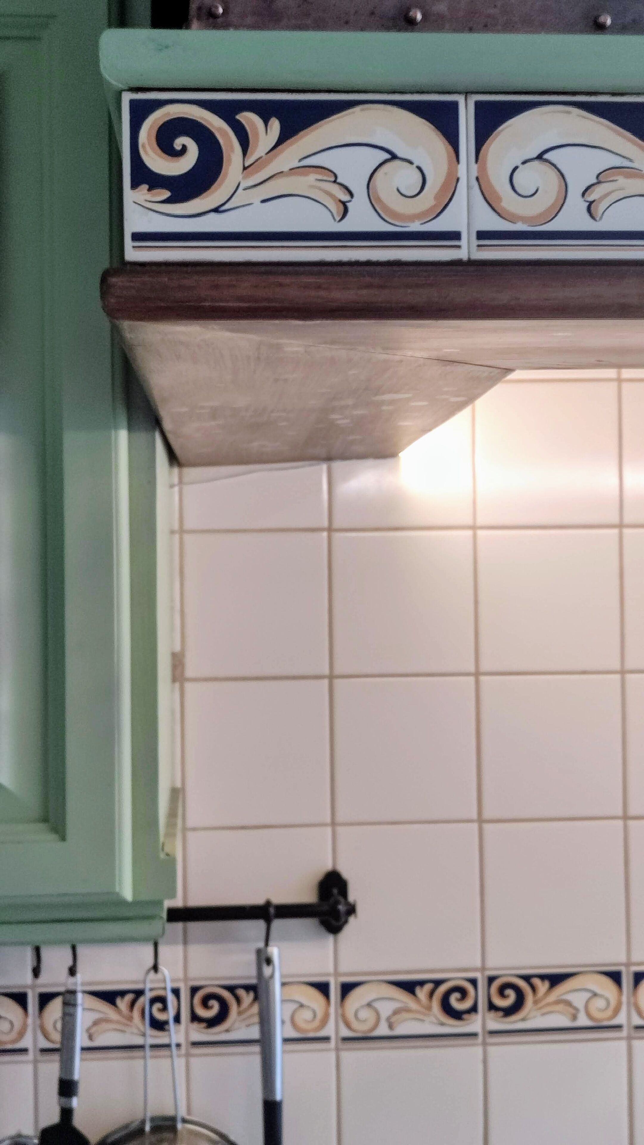 Una cocina con baldosas blancas, un gabinete verde y un detalle decorativo en los azulejos.