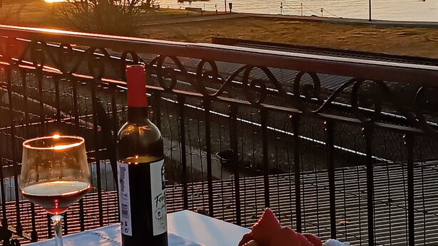 A table with a bottle of wine, a glass, and a plate of strawberries and cream on a balcony overlooking a body of water and a distant hill. - Donna Nega Guest House  (Caminha)