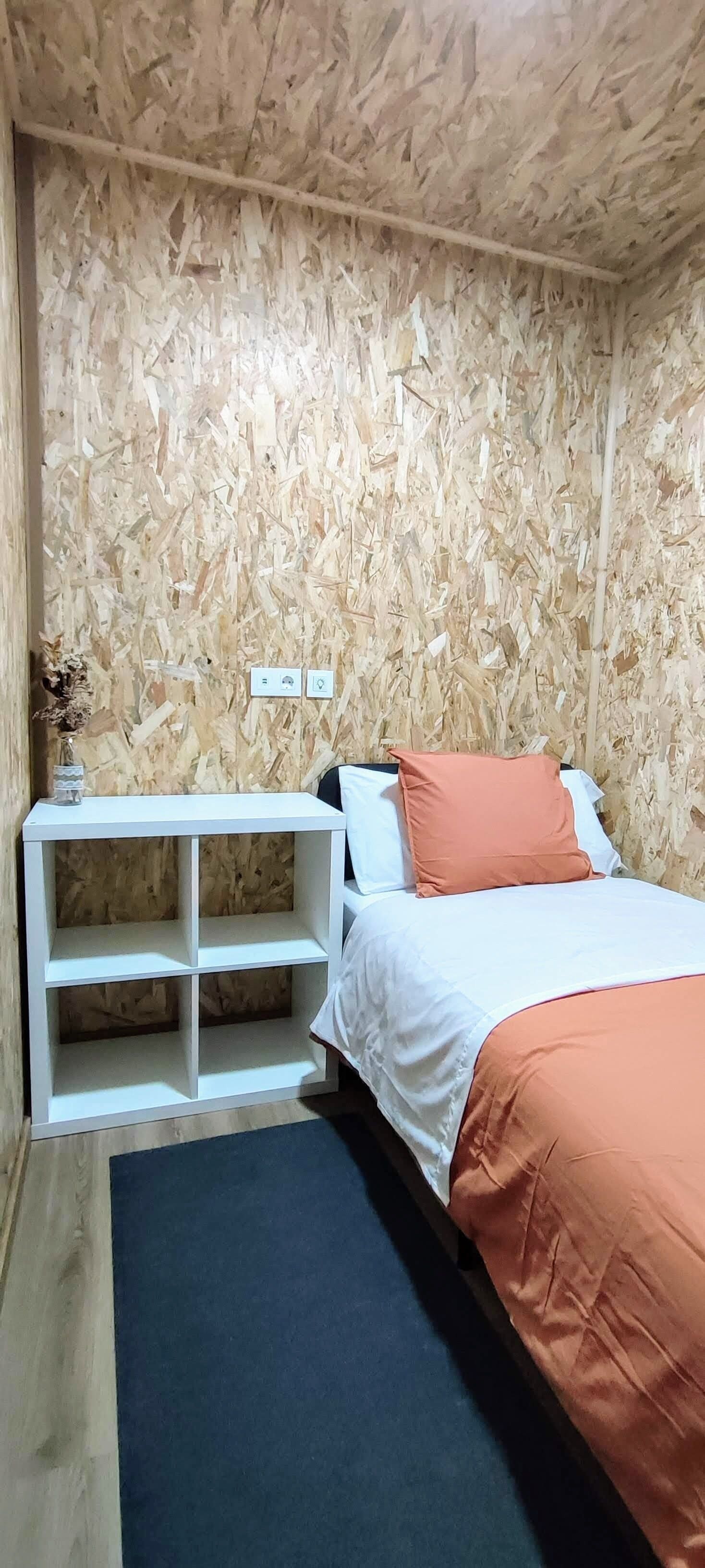 Una habitación con una cama, mesitas de noche blancas, una consola blanca y un tapete oscuro.