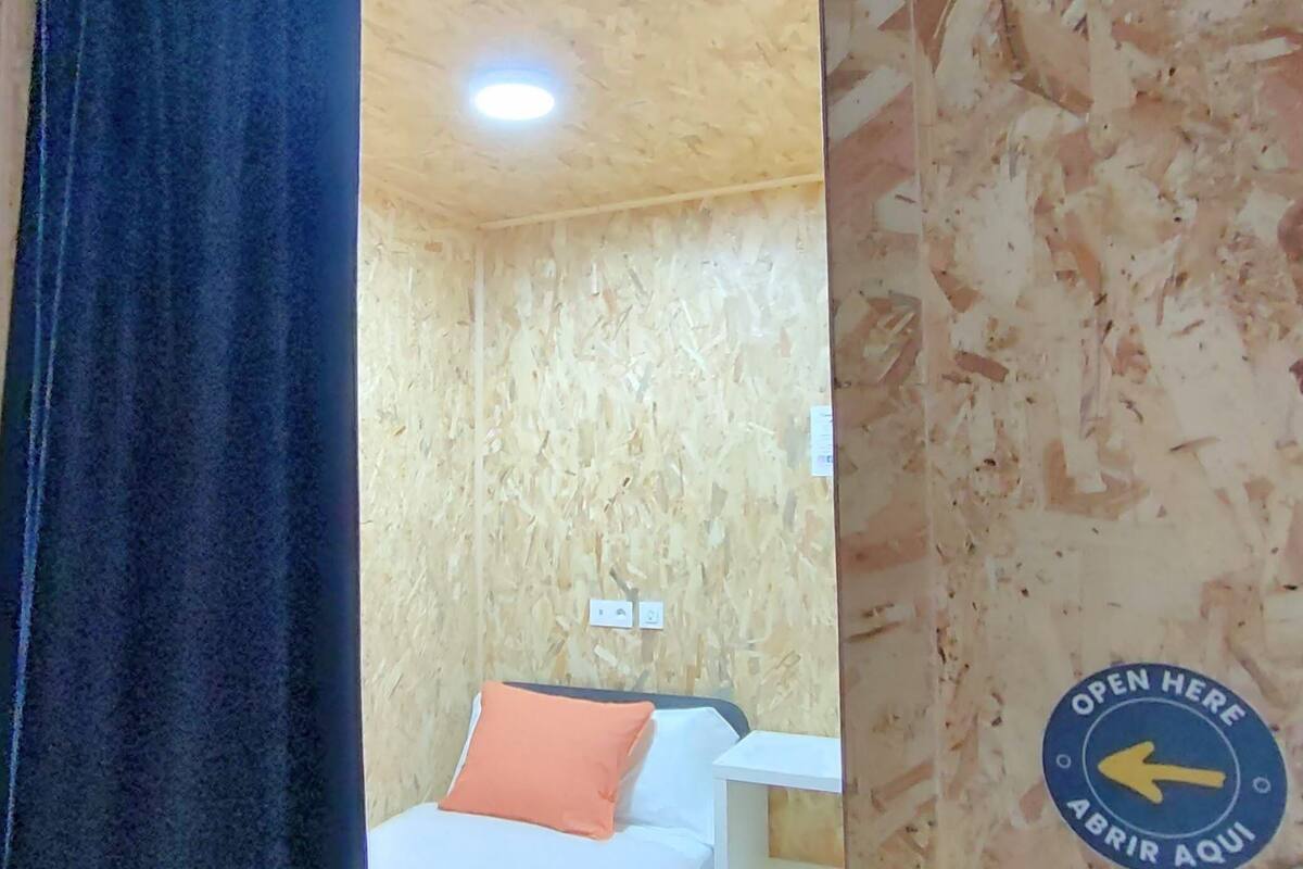 A room with wooden walls, a bed with an orange pillow, and a sign indicating the room is open.