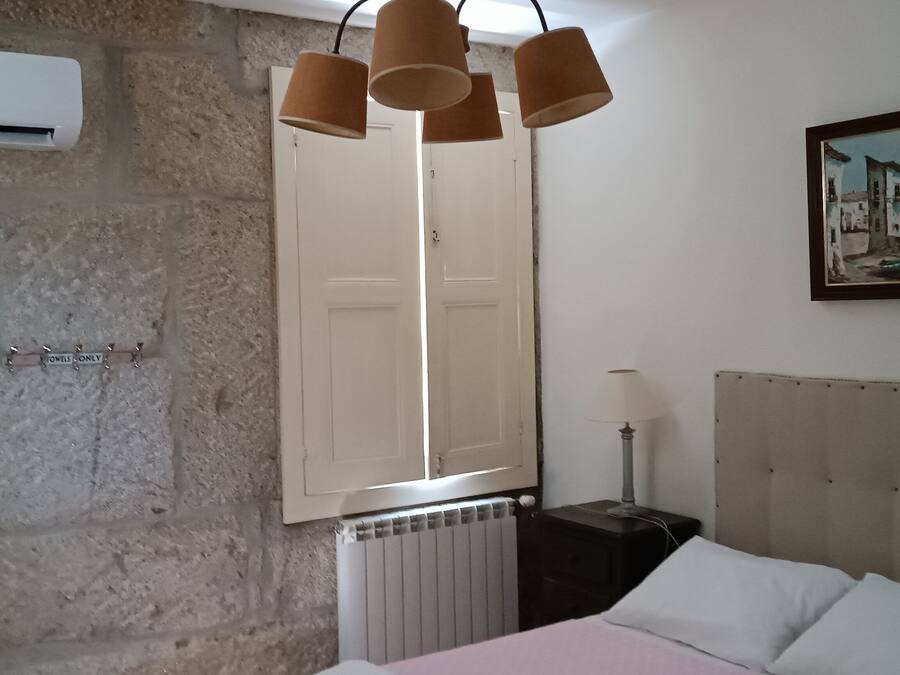 Un dormitorio con pared de piedra, una cama con cabecera capitonada, un cuadro, un radiador y una lámpara colgante.