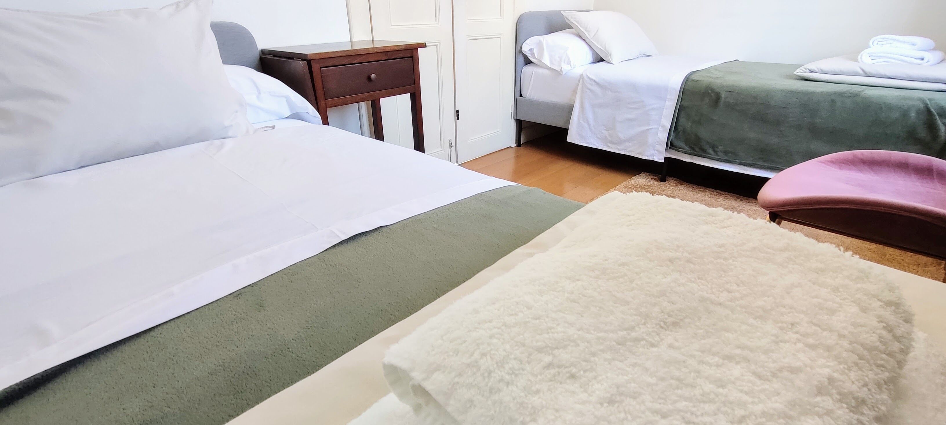 A hotel room with two beds, a small wooden nightstand, a chair, and a green bedspread.