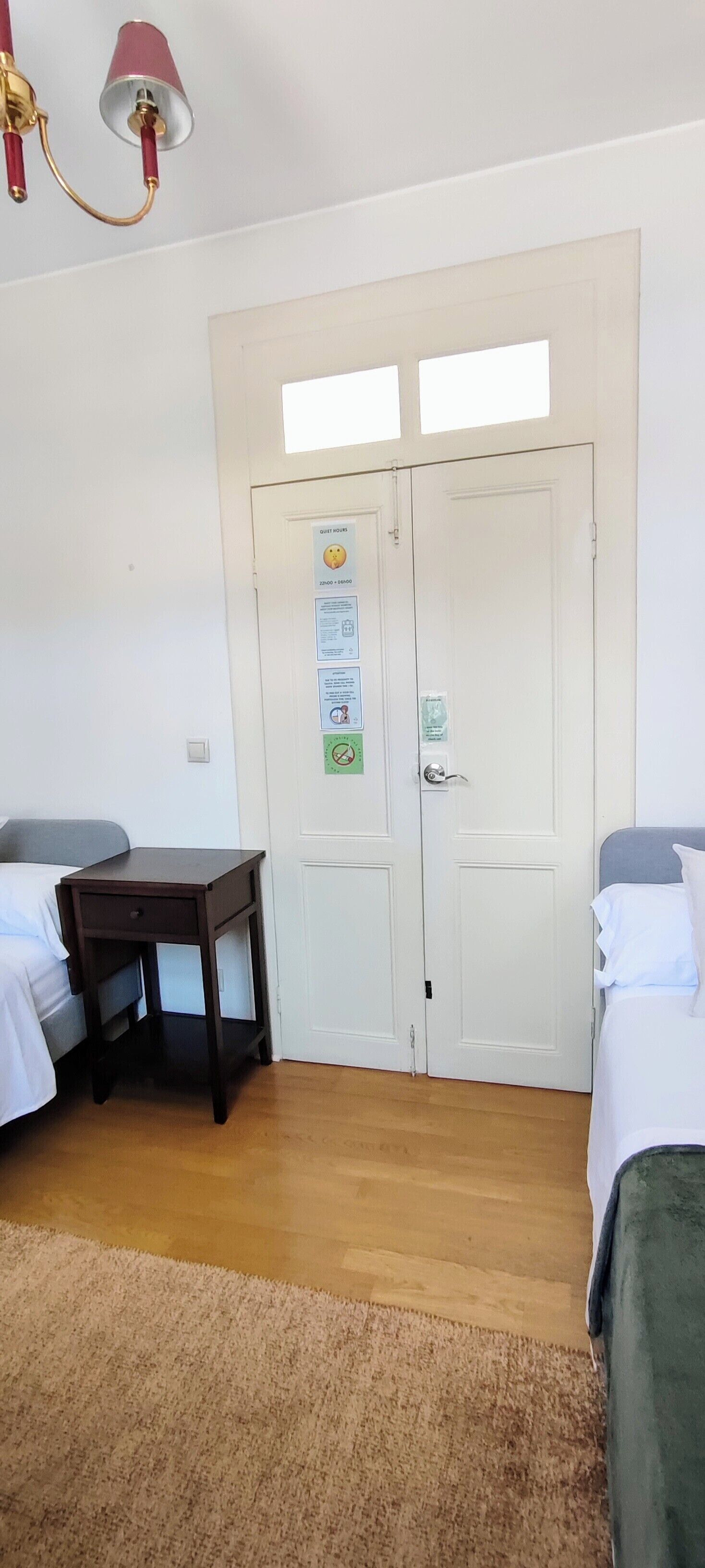 A bedroom with two beds, a wooden nightstand, a desk, and a white door with a window.