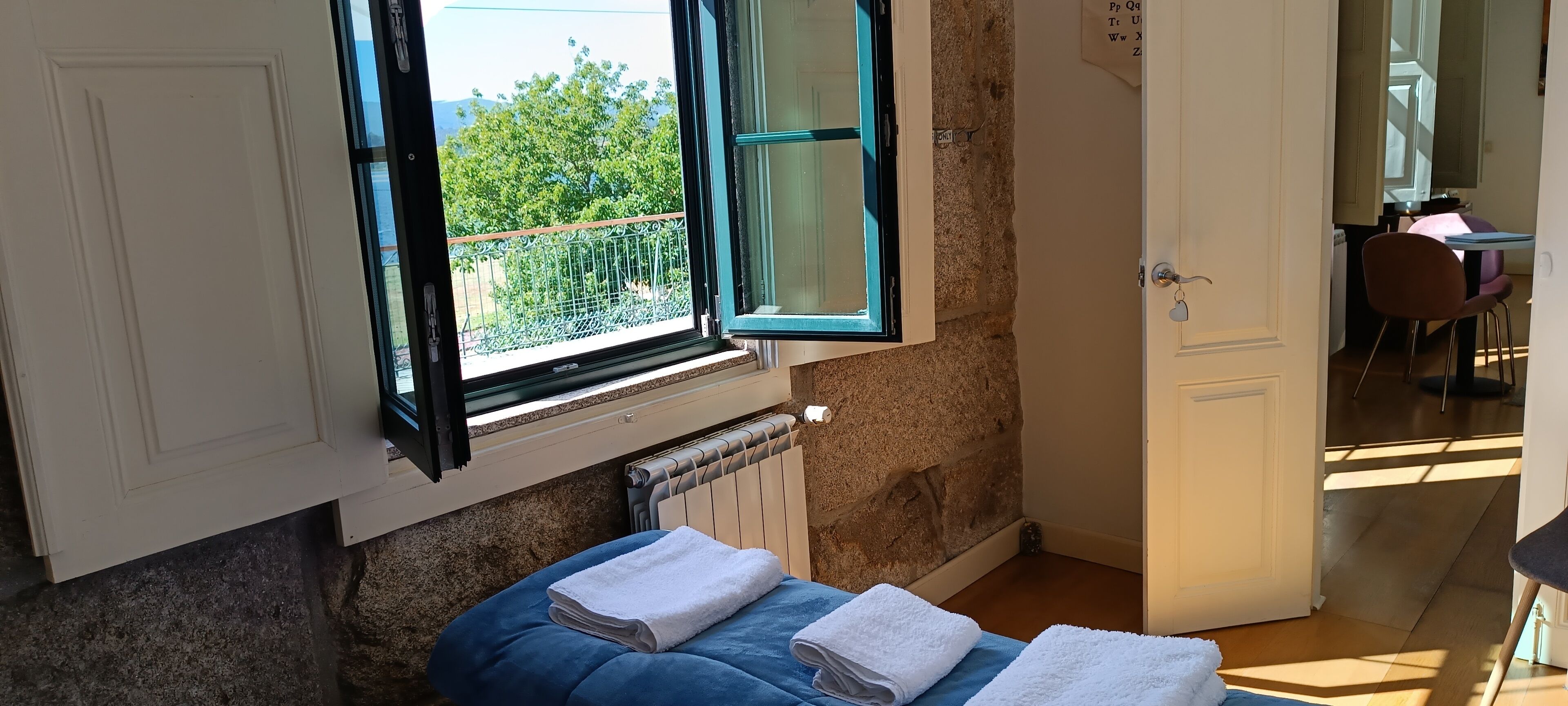 Een kleine kamer met een raam, een radiator, een blauwe bank en een deur naar een andere kamer.