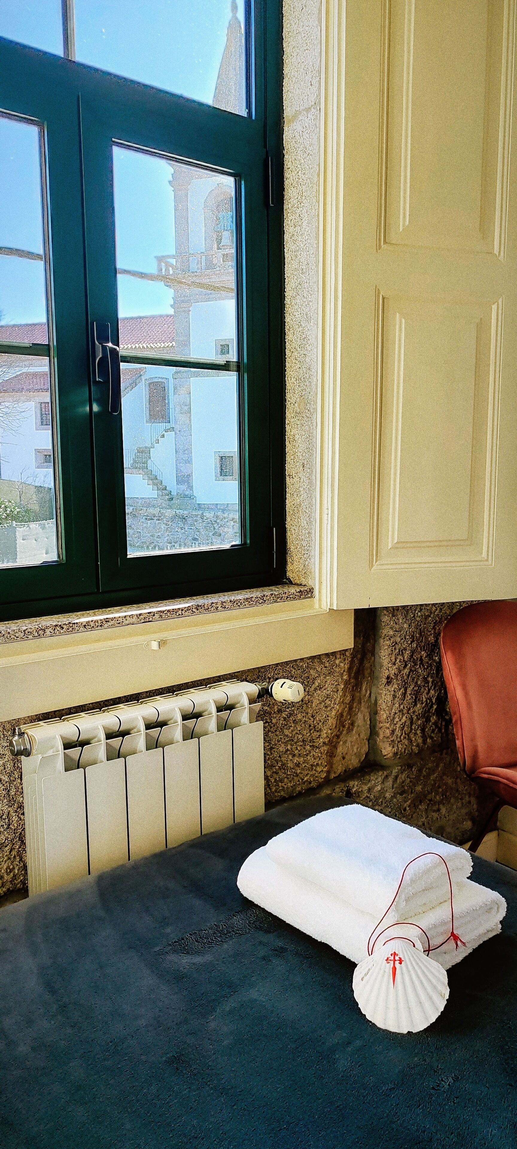 A bathroom with a window, a radiator, a towel, and a red towel on the counter.
