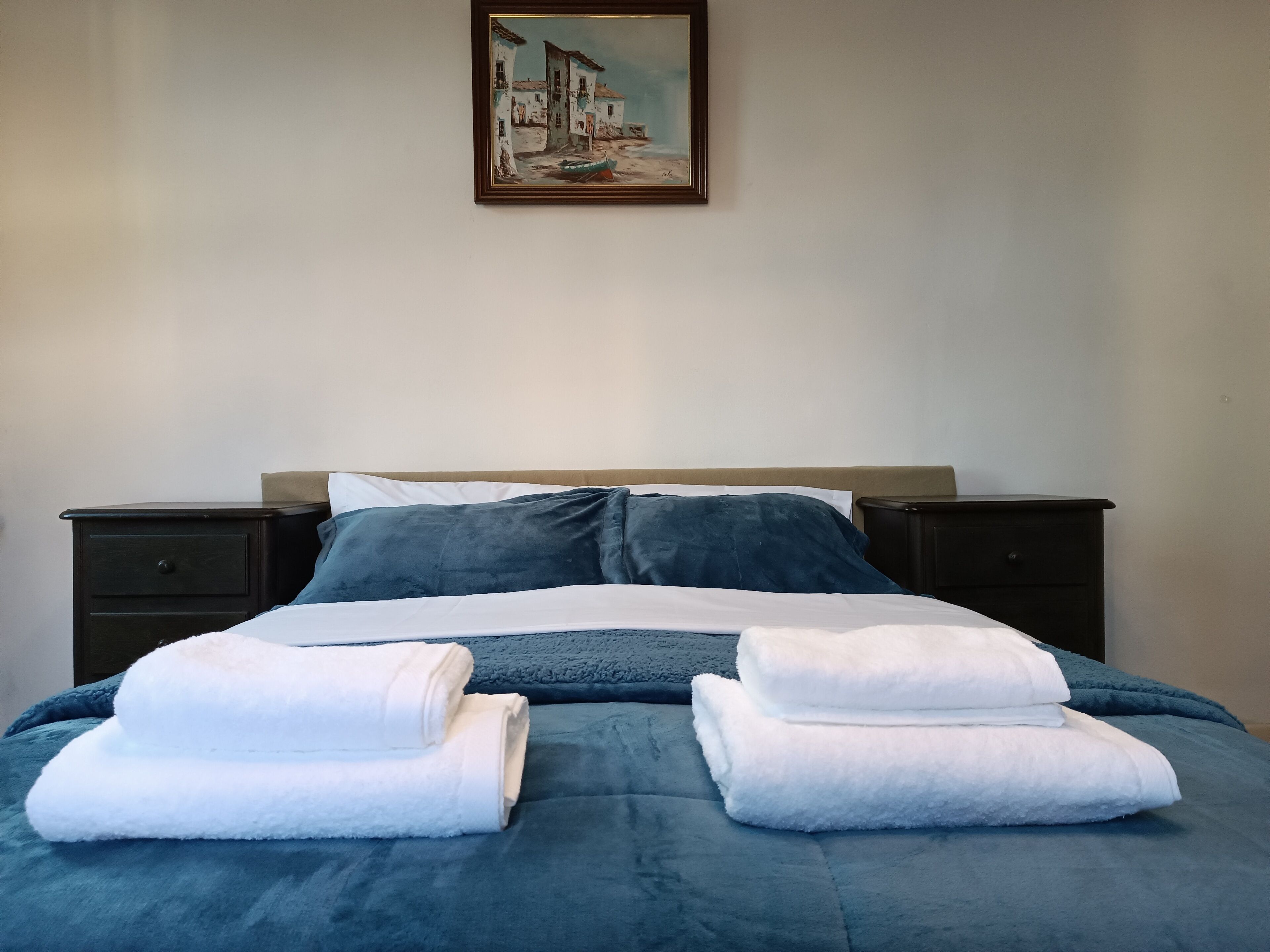 Una cama bien hecha con ropa de cama azul, almohadas blancas y dos toallas blancas dobladas.