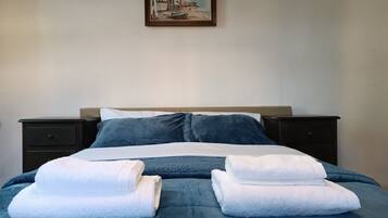 Una cama bien hecha con ropa de cama azul, almohadas blancas y dos toallas blancas dobladas.