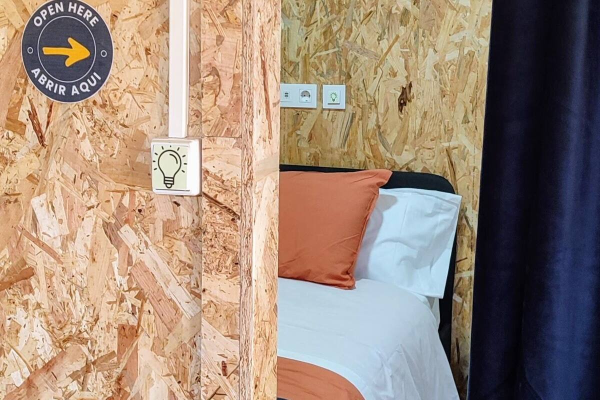 A room with a bed, a light switch, and a door marked with the number 6.