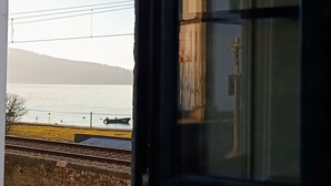 A view from a window overlooking a body of water, a distant building, and a railway track. - Donna Nega Guest House  (Caminha)