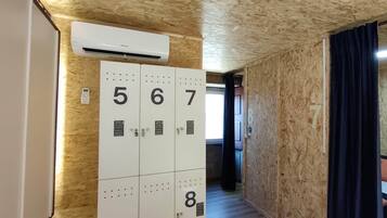 Un pasillo de hotel con taquillas numeradas, un equipo de aire acondicionado y una cama con cortina oscura.