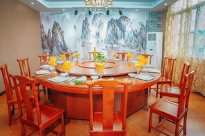 A round dining table with chairs, a chandelier, and a wall mural. - Friendly Hotel (Shaoguan Nanhua Temple) (Shaoguan)