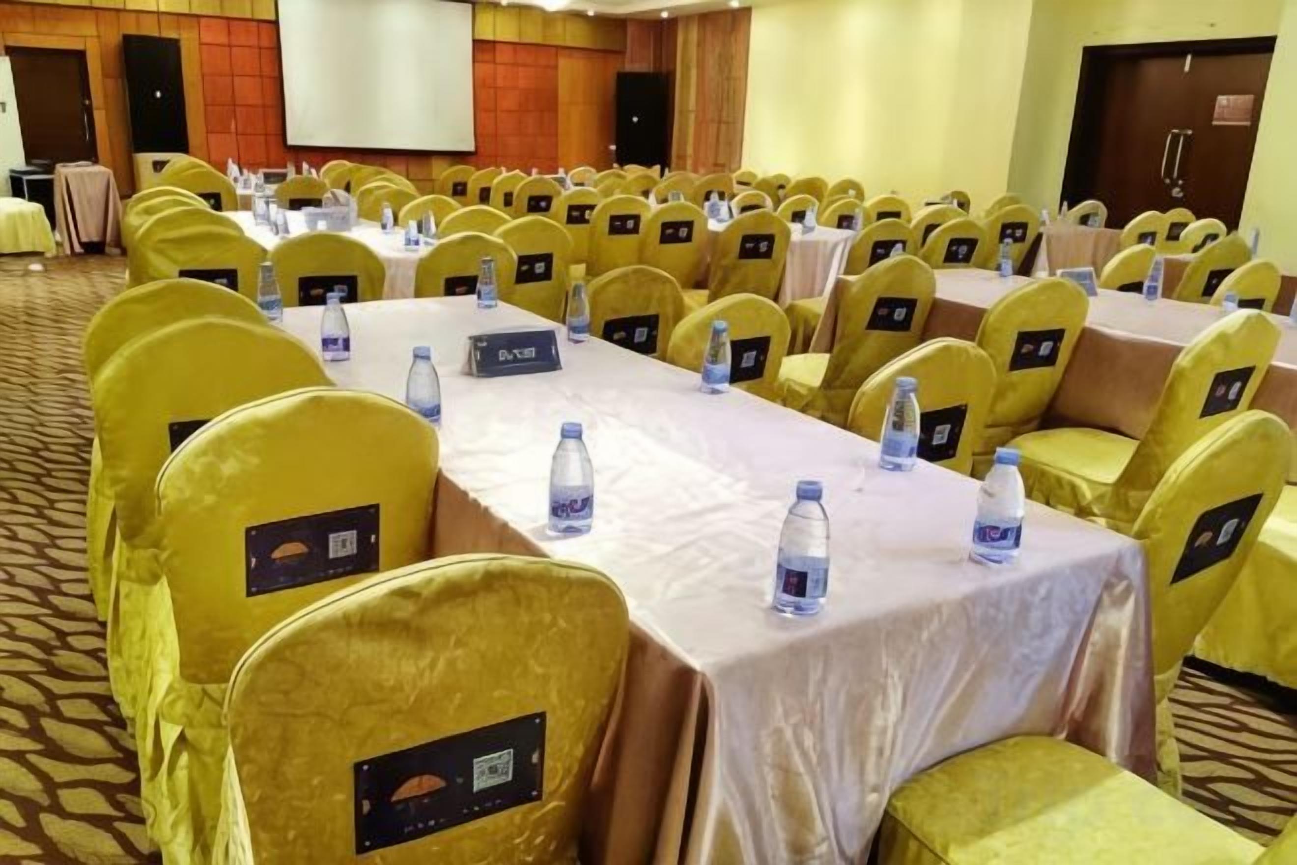 Un salón de conferencias con hileras de sillas amarillas, mesas con tarjetas de identificación y botellas de agua.
