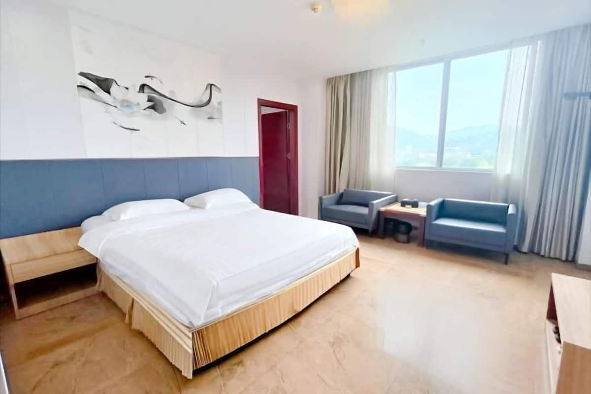 Habitació d'hotel amb un llit, escriptori, cadira, sofà, finestra amb cortines i una obra d'art a la paret.