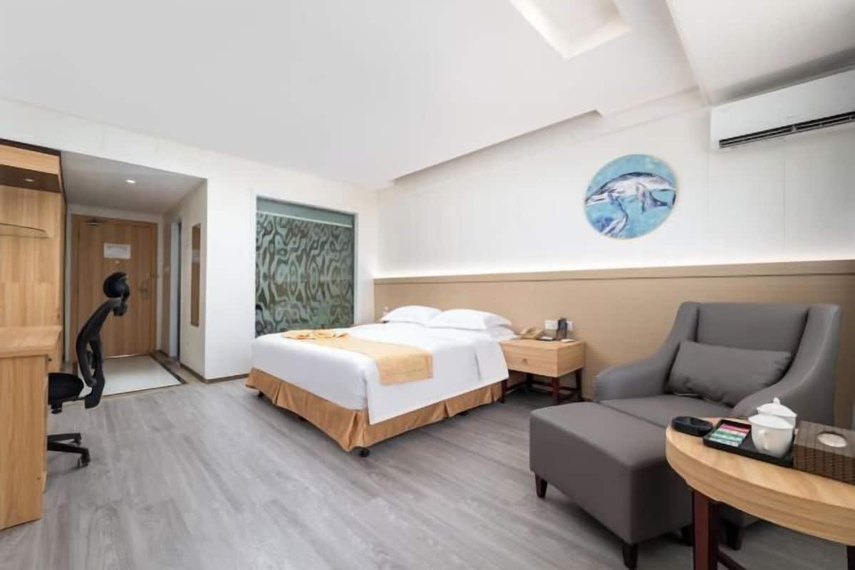 Habitació d'hotel amb un llit, una taula de treball, una cadira, una taula petita i una pintura penjada a la paret.