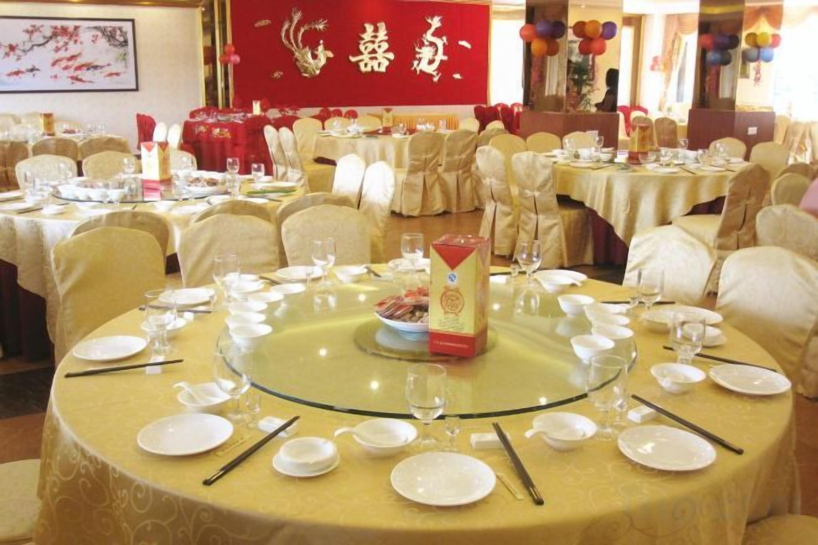 A banquet hall with round tables set for a formal event, featuring a central red banner with gold lettering.
