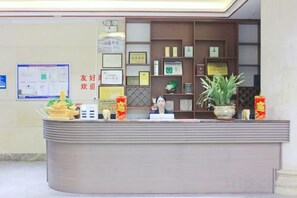 A reception desk with a counter, a potted plant, and various framed certificates or awards on the wall behind.
