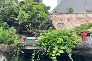 A rock garden with greenery and a brick wall with red text. - Friendly Hotel (Shaoguan Nanhua Temple) (Shaoguan)