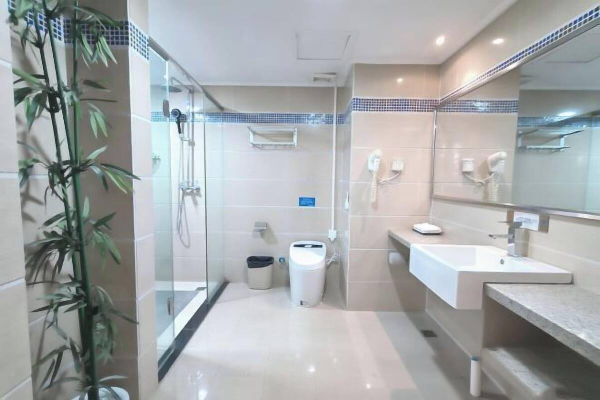 Un bany modern amb un espai de dutxa de vidre, un lavabo blanc i un mirall gran.