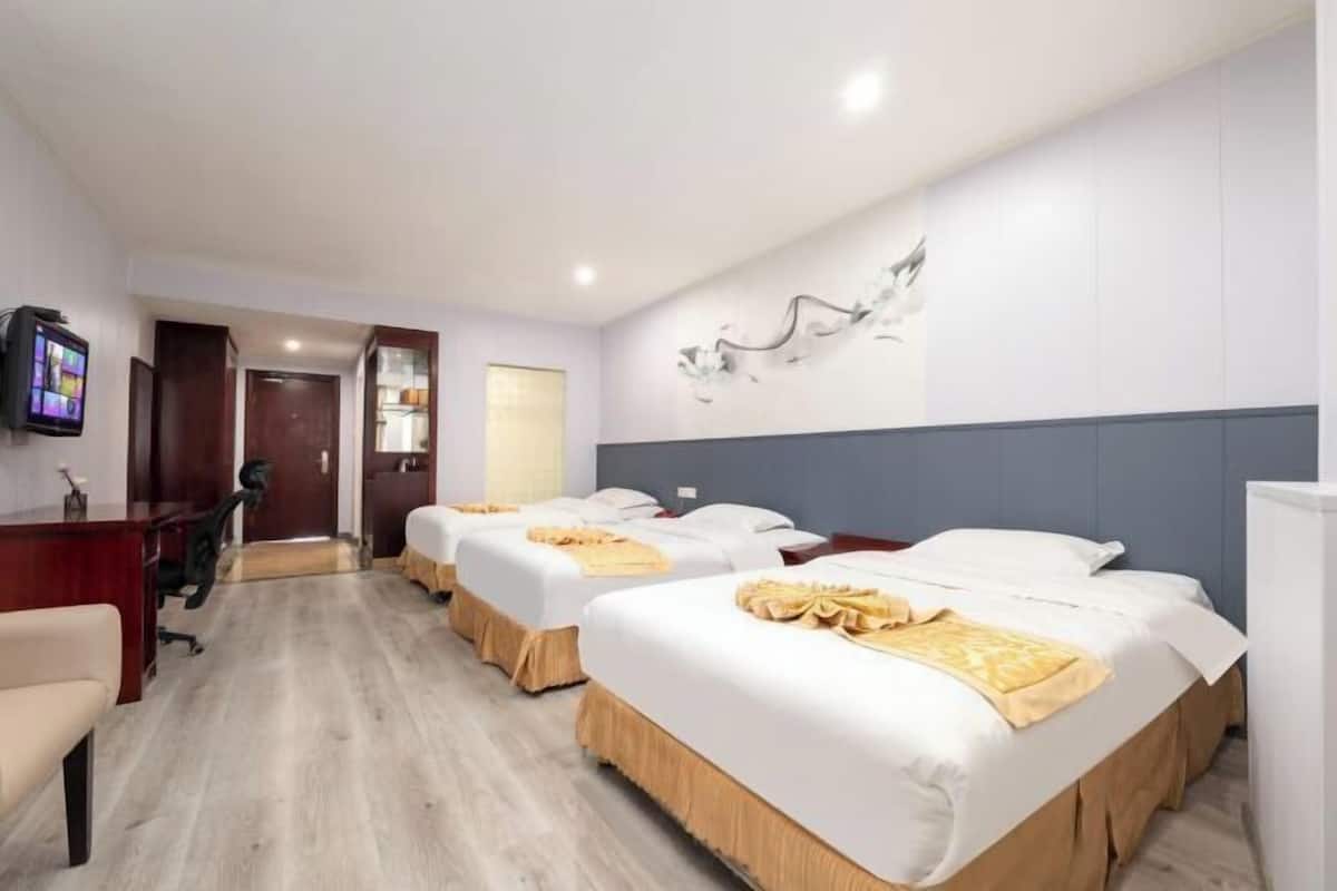 Habitació d'hotel amb tres llits, una taula, una cadira i una televisió.